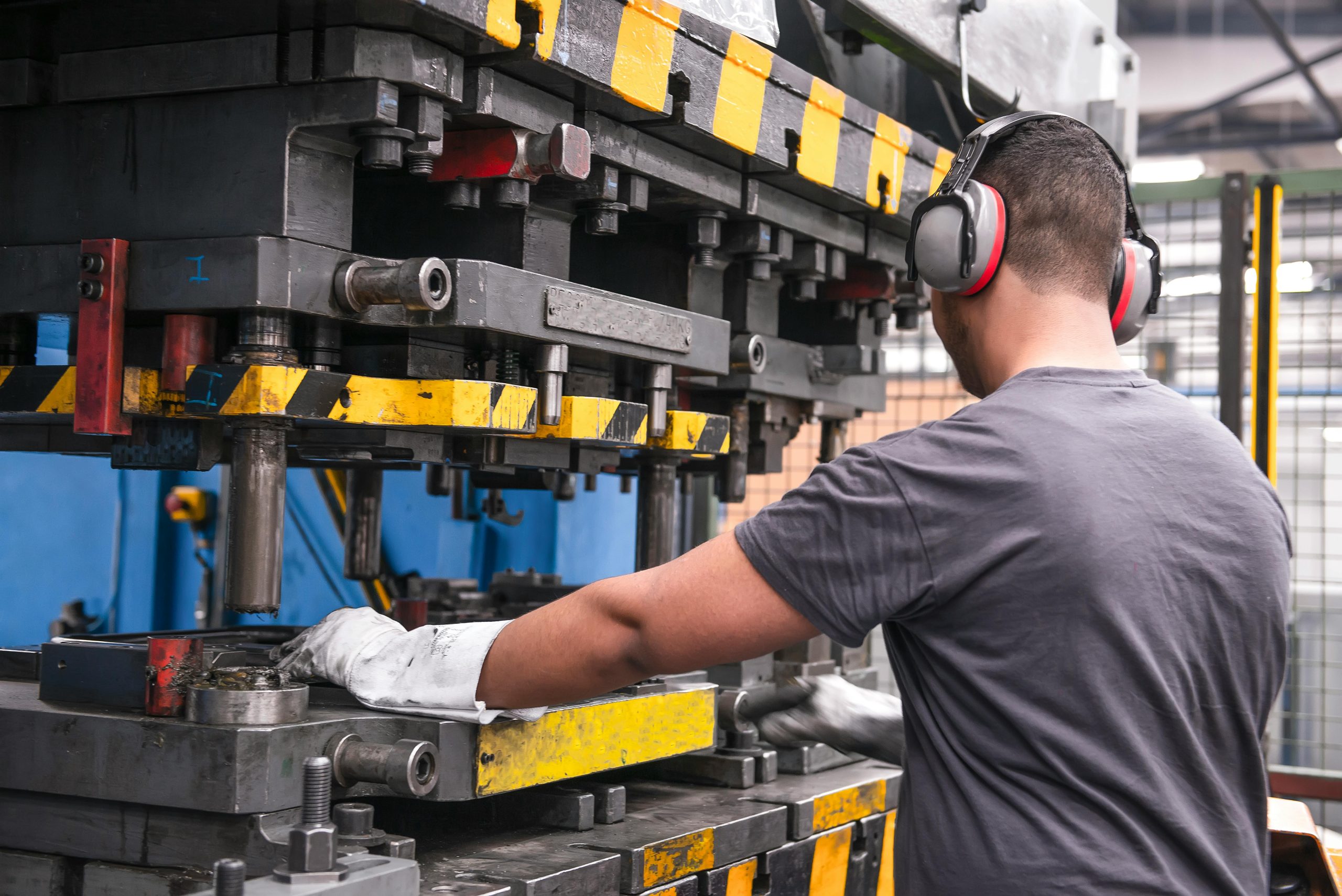 A man at a large factory machine wearing gloves and hearing protection