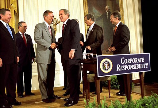 A group of men in suits shaking hands behind a podium that says "corporate responsibility"