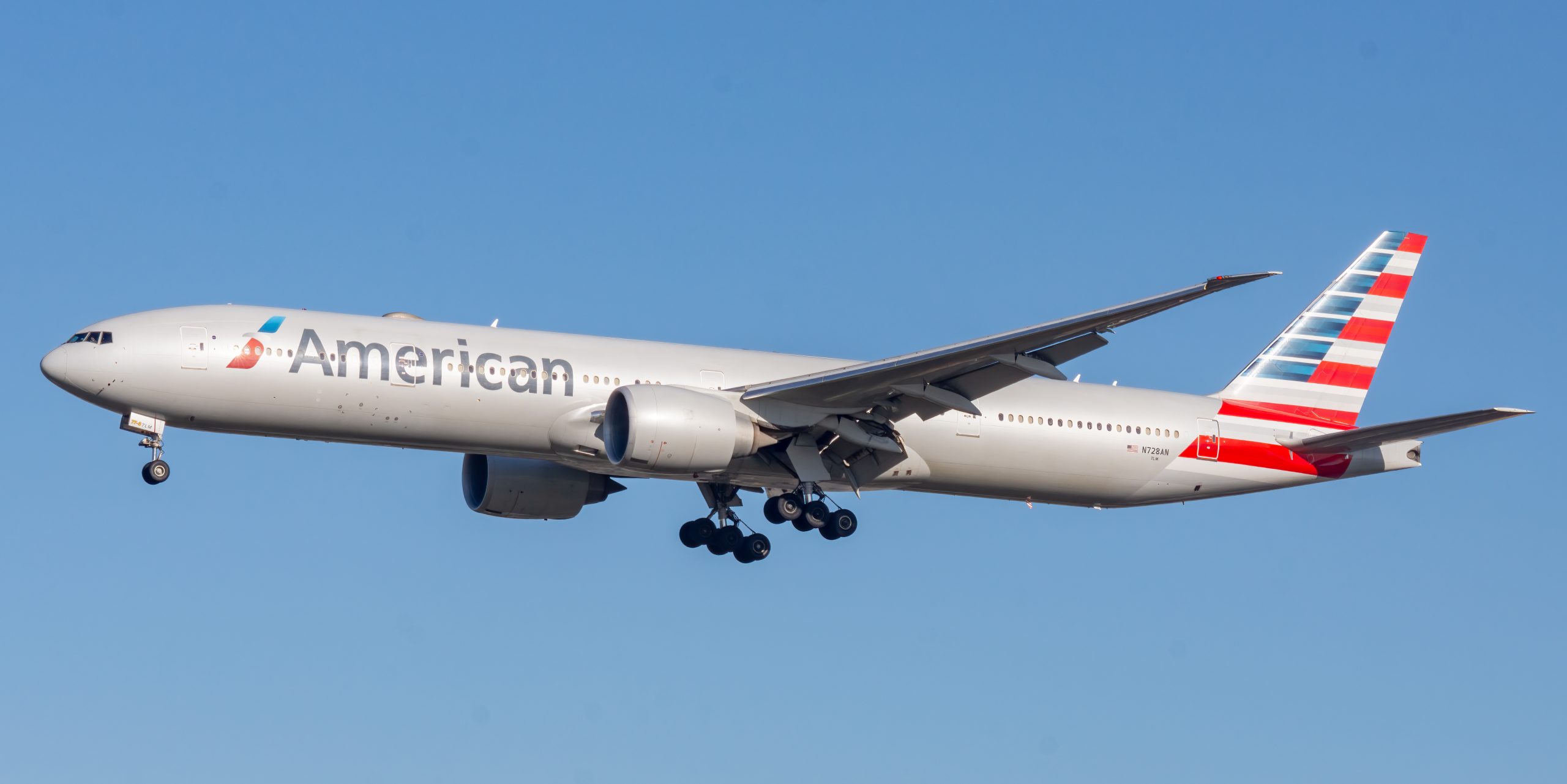 American Airlines jet in midair against a clear blue sky with landing gear extended.